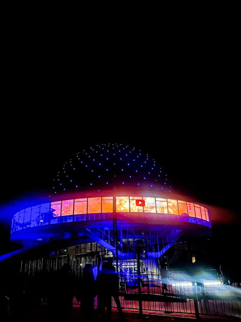 Illuminated dome of the Buenos Aires Planetarium glowing with blue lights at night while colorful projections light up the windows around the circular building. Futuristic landmark in Palermo parks often visited in the evening during a 2 days in Buenos Aires itinerary.